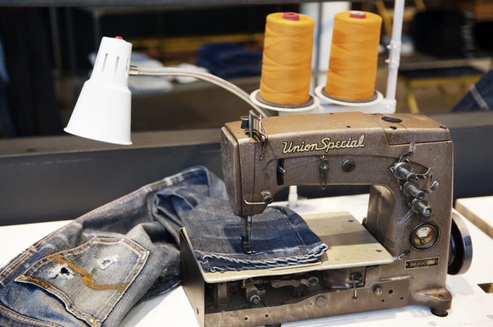Nudie Jeans a pair on a sewing machine being fixed